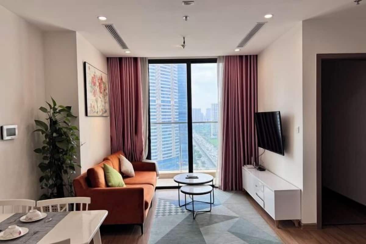 Uma sala de estar moderna com sofá, mesa de jantar, televisão e uma grande janela com cortinas.