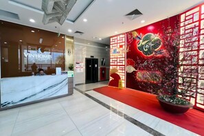 Un hall d’accueil d’hôtel avec un comptoir en marbre, une moquette rouge et un mur décoratif aux couleurs rouge et or.