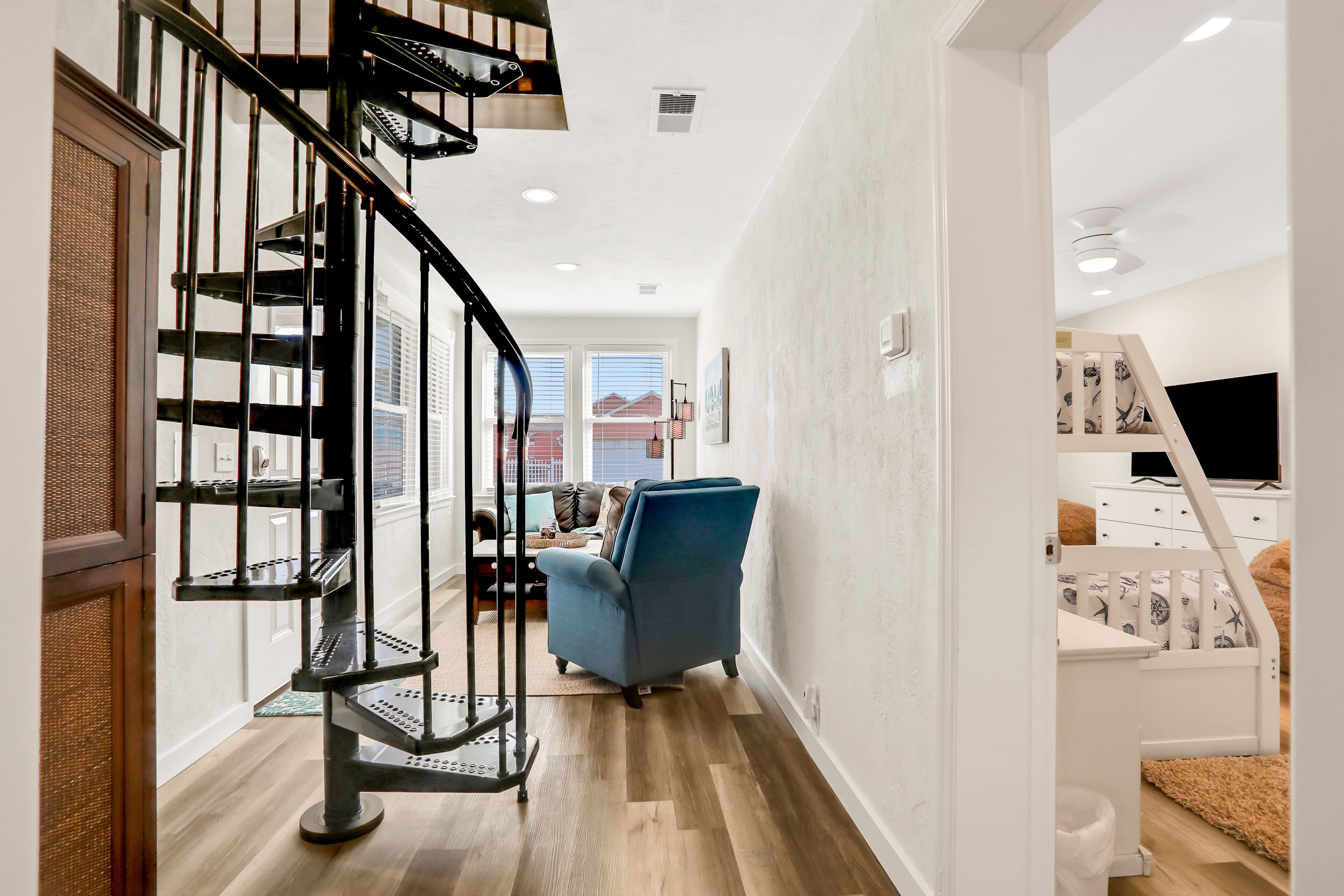 Un intérieur moderne avec un escalier en colimaçon, un fauteuil bleu et une commode blanche.