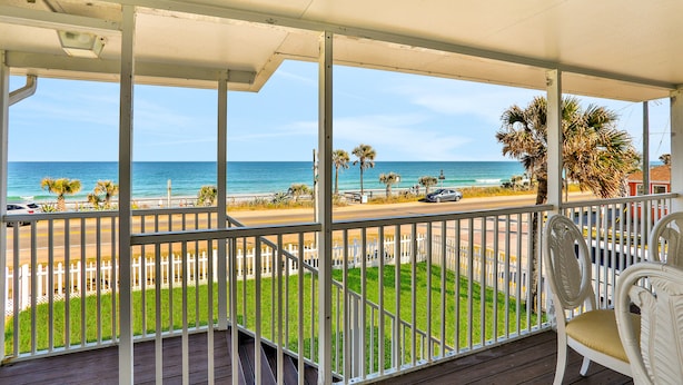 A covered balcony with a view of the beach and ocean.