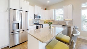 A modern kitchen with white cabinetry, stainless steel appliances, and a central island with seating. - Stylish brand-new ocean view home with deck & porch - steps to beach (Palm Coast)
