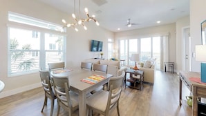 A spacious living area with a dining table, sofas, and a ceiling fan. - Stylish brand-new ocean view home with deck & porch - steps to beach (Palm Coast)