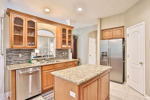 A modern kitchen with wooden cabinets, granite countertops, stainless steel appliances, and a tiled backsplash. - Wonderful coastal home with WiFi, enclosed backyard, screened patio (Palm Coast)