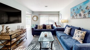 A modern living room with a dark blue sofa, a glass coffee table, and a wooden sideboard. - Water-view dog-friendly home with outdoor space & entertainment options (Palm Coast)
