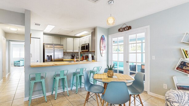 A modern kitchen with stainless steel appliances, a central island with bar stools, and a dining area with a wooden table and chairs. - Water-view dog-friendly home with outdoor space & entertainment options (Palm Coast)
