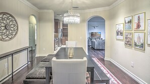 A dining area with a chandelier, a long table, and a bench. There are framed pictures on the walls and a decorative wall piece.