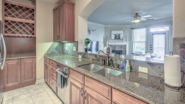 A kitchen with granite countertops, wooden cabinets, a double sink, and a ceiling fan.