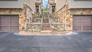 A stone staircase leading to a gated entrance with two garages, surrounded by a paved driveway.