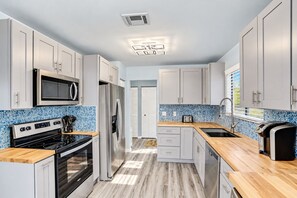 A modern kitchen with stainless steel appliances, a wooden countertop, and a blue mosaic backsplash. - Charming home near beach & golf with central AC & patio - dog-friendly (Palm Coast)