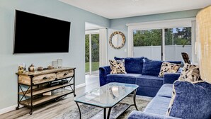 A living room with a blue sofa, a glass coffee table, and a wooden side table with decorative items.