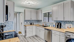 A modern kitchen with white cabinets, a wooden countertop, a dishwasher, and a coffee maker.