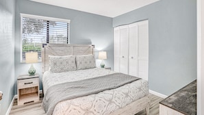 A bedroom with a bed, nightstands, a window with blinds, and a wardrobe.