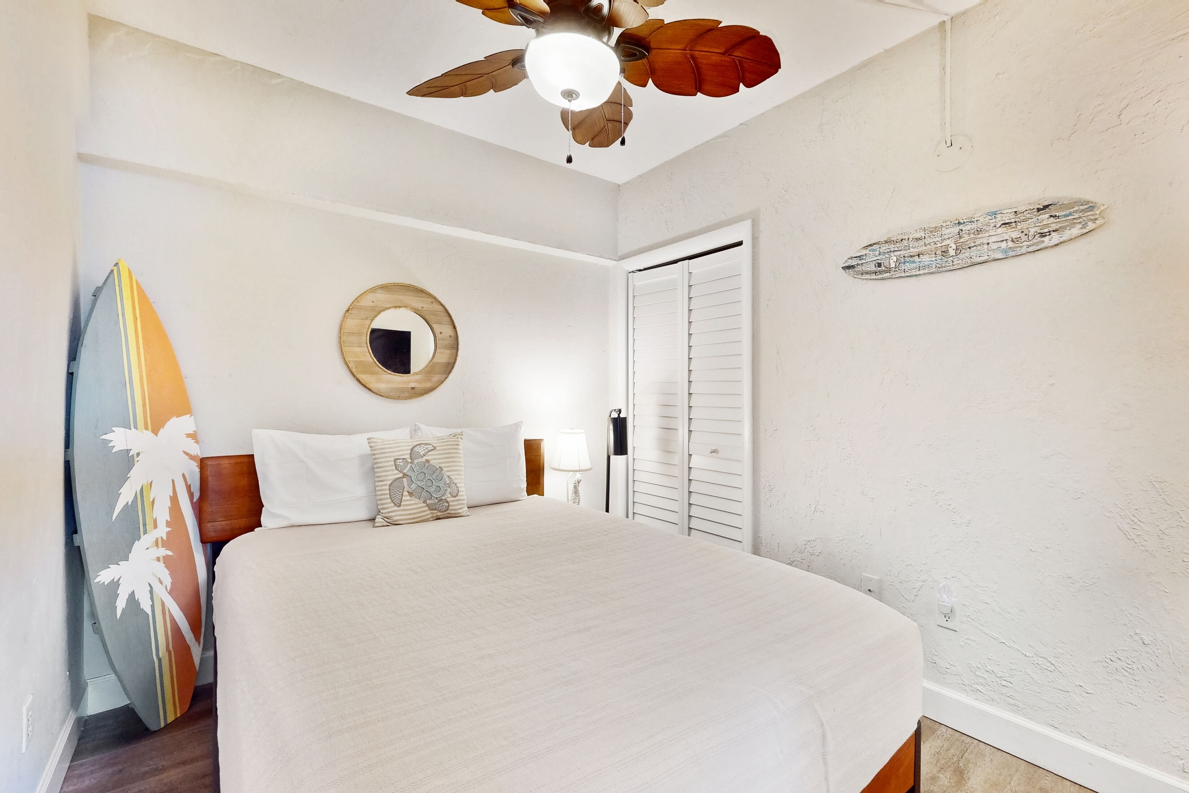 Un dormitorio con una cama grande, un ventilador de techo, un espejo en la pared y una decoración con una tabla de surf.