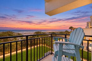 A balcony with a view of the beach and ocean during sunset.