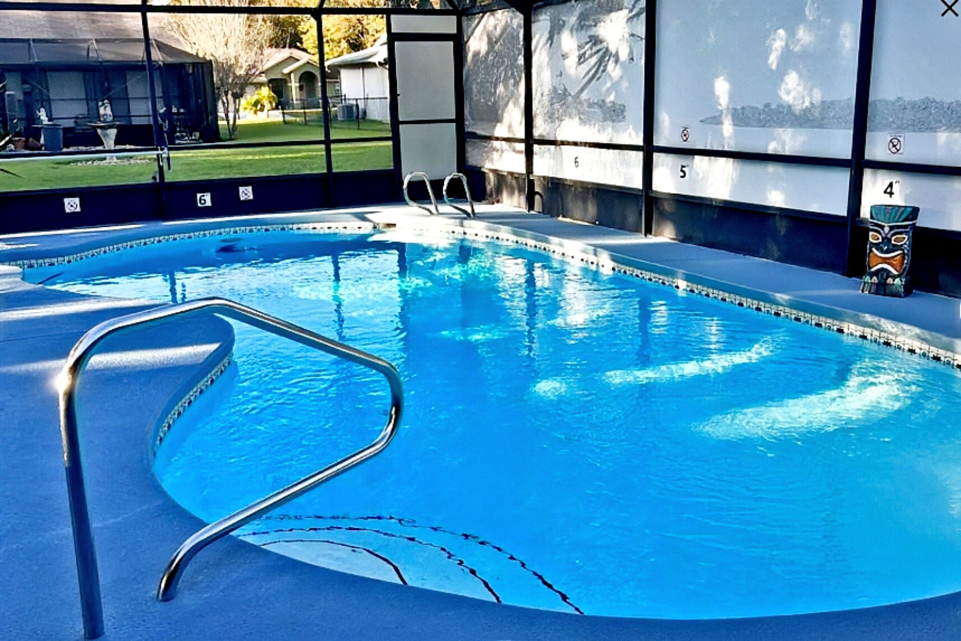 An indoor swimming pool with clear blue water, a metal ladder, and a view of a golf course through large windows.