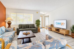 Un salon avec un canapé, une table basse, un téléviseur et une plante.