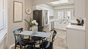 A modern kitchen with white cabinets, a stainless steel refrigerator, and a dining area with a glass table and chairs. - Oceanfront condo with large patio, direct water access, pool, central AC, & W/D (Palm Coast)