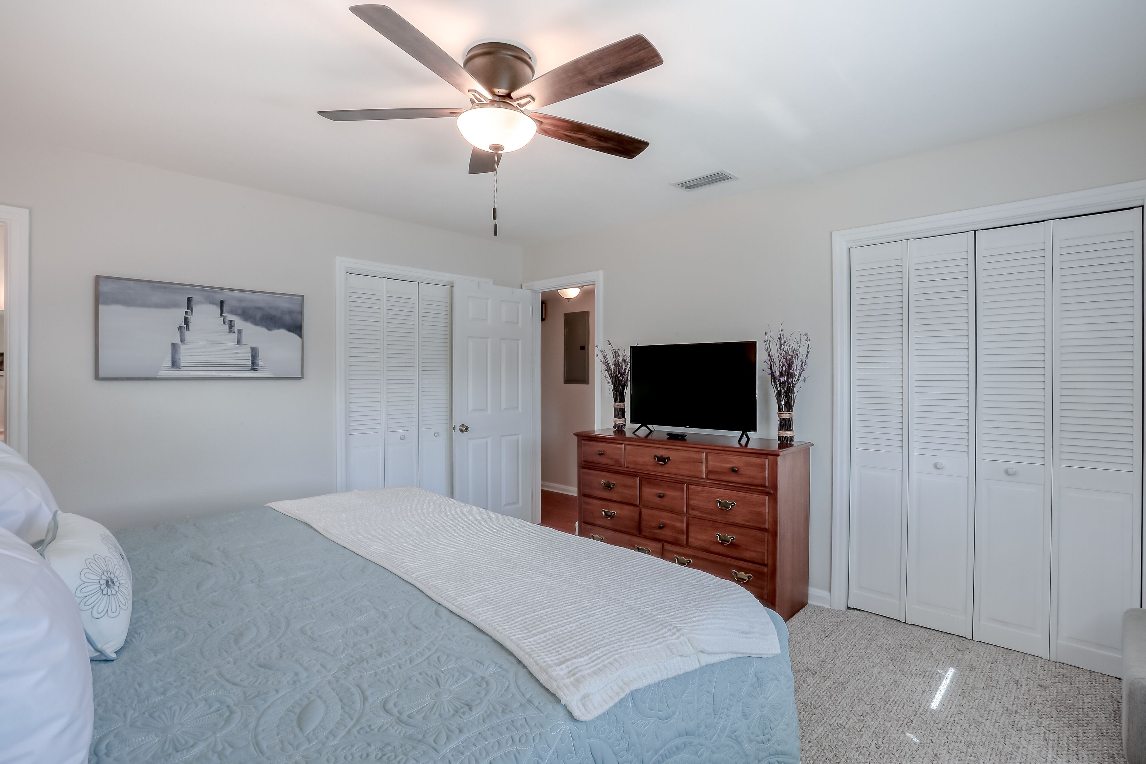 A bedroom with a bed, a ceiling fan, a dresser, a TV, and a closet.