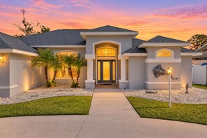 A modern two-story house with a well-lit entrance, a driveway, and a landscaped front yard.