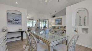 A spacious dining area with a glass-top table, wicker chairs, and a chandelier. - Contemporary coastal escape with heated pool, fenced yard, & outdoor dining (Palm Coast)