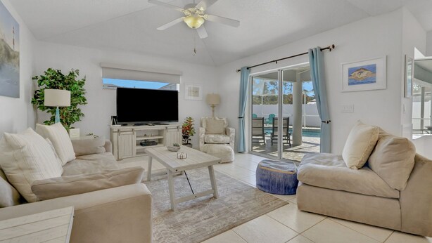 A modern living room with a flat-screen TV, a ceiling fan, and a large sliding glass door leading to an outdoor area. - Contemporary coastal escape with heated pool, fenced yard, & outdoor dining (Palm Coast)