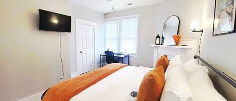 Ein Hotelzimmer mit Bett, Schreibtisch, Deckenventilator, Fernseher und einem Fenster mit Jalousien.