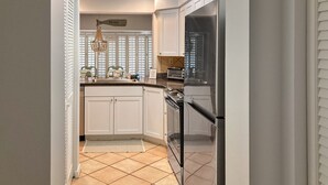 Cocina compacta con gabinetes blancos, refrigerador negro, horno empotrado y lámpara colgante.