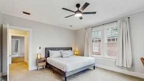 Een slaapkamer met een bed, nachtlampjes, een plafondventilator en een raam met gordijnen.