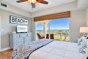 A bedroom with a large bed, a television, a view of the beach, and a balcony with chairs. - Ocean view condo with pool access, WiFi, & central AC - snowbirds OK (Palm Coast)