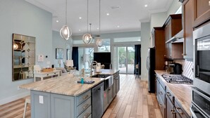 Une cuisine moderne dotée d’un grand îlot central, d’appareils électroménagers en acier inoxydable et de luminaires suspendus.