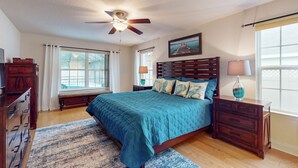 A bedroom with a bed, wooden headboard, nightstands, a ceiling fan, and a large window with curtains. - Spacious Home with Private Pool,Spa, Gas Grill and Patio (Palm Coast)