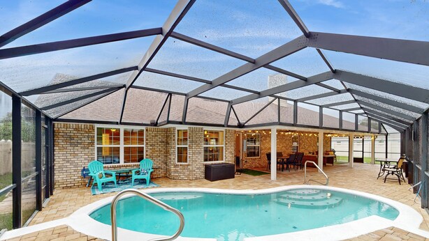 A covered outdoor swimming pool with a brick patio, seating area, and a glass enclosure. - Spacious Home with Private Pool,Spa, Gas Grill and Patio (Palm Coast)