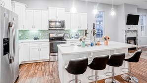 A modern kitchen with white cabinets, stainless steel appliances, a central island with bar stools, and pendant lighting. - Updated, dog-friendly gem w/fenced yard, foosball & pool tables, WiFi, fireplace (St. Augustine)