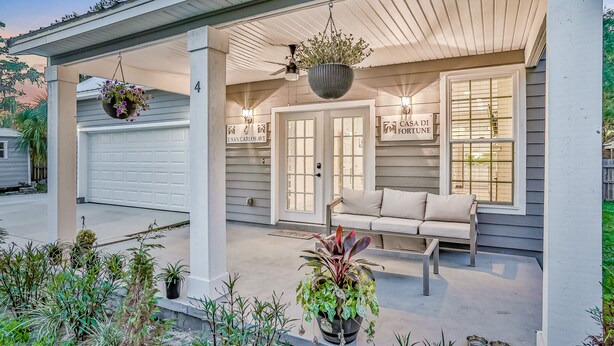 A covered porch with a white garage door, a hanging planter, a sofa, and a sign reading "Casa Di Fortuna." - Updated, dog-friendly gem w/fenced yard, foosball & pool tables, WiFi, fireplace (St. Augustine)