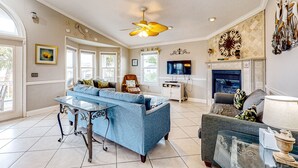 A spacious living room with a blue sofa, a glass coffee table, a fireplace, and a ceiling fan.