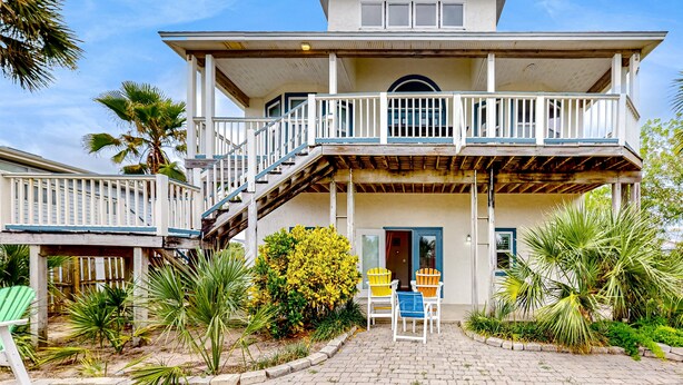 A two-story house with a covered porch, a staircase, and a small garden with chairs and plants.