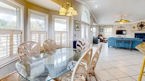 A spacious living area with a glass-top dining table surrounded by wicker chairs, a blue sofa, and a television.