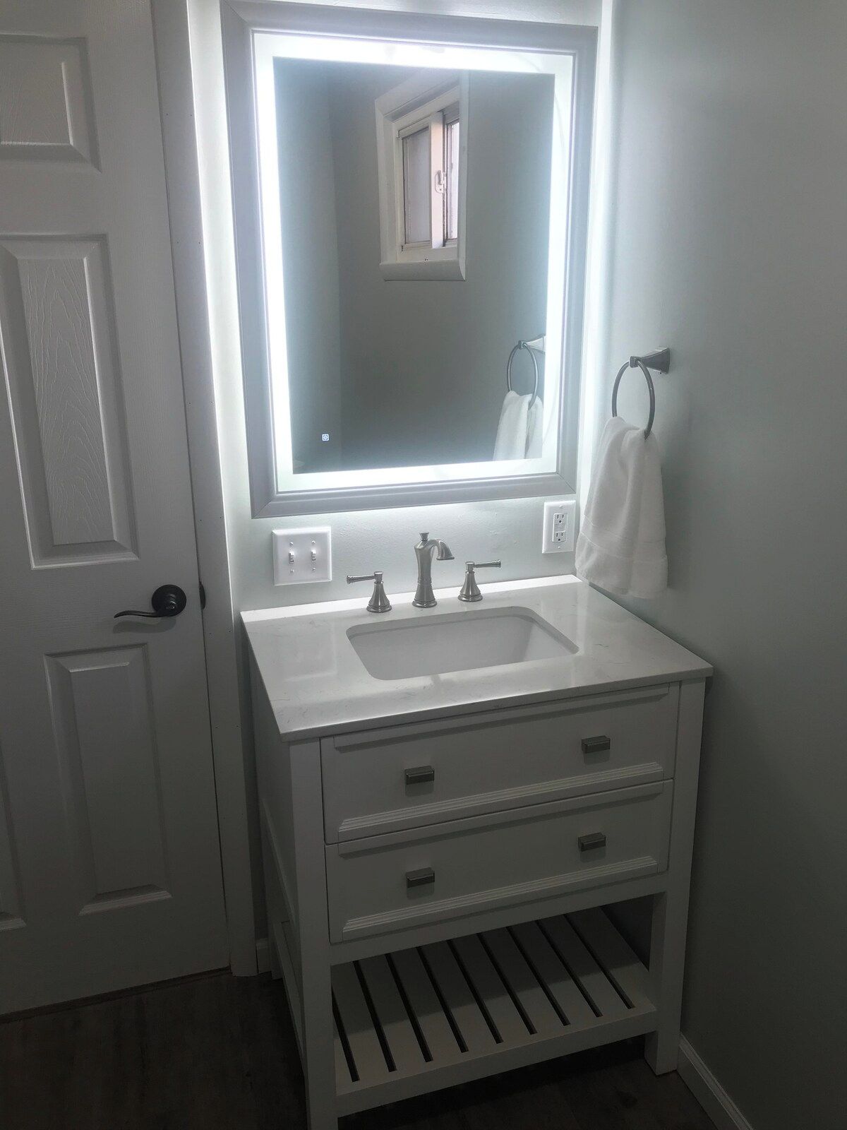 A bathroom with a white vanity, a mirror, a sink, and a towel rack.