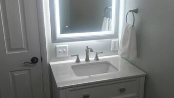 A bathroom with a white vanity, a mirror, a sink, and a towel rack.