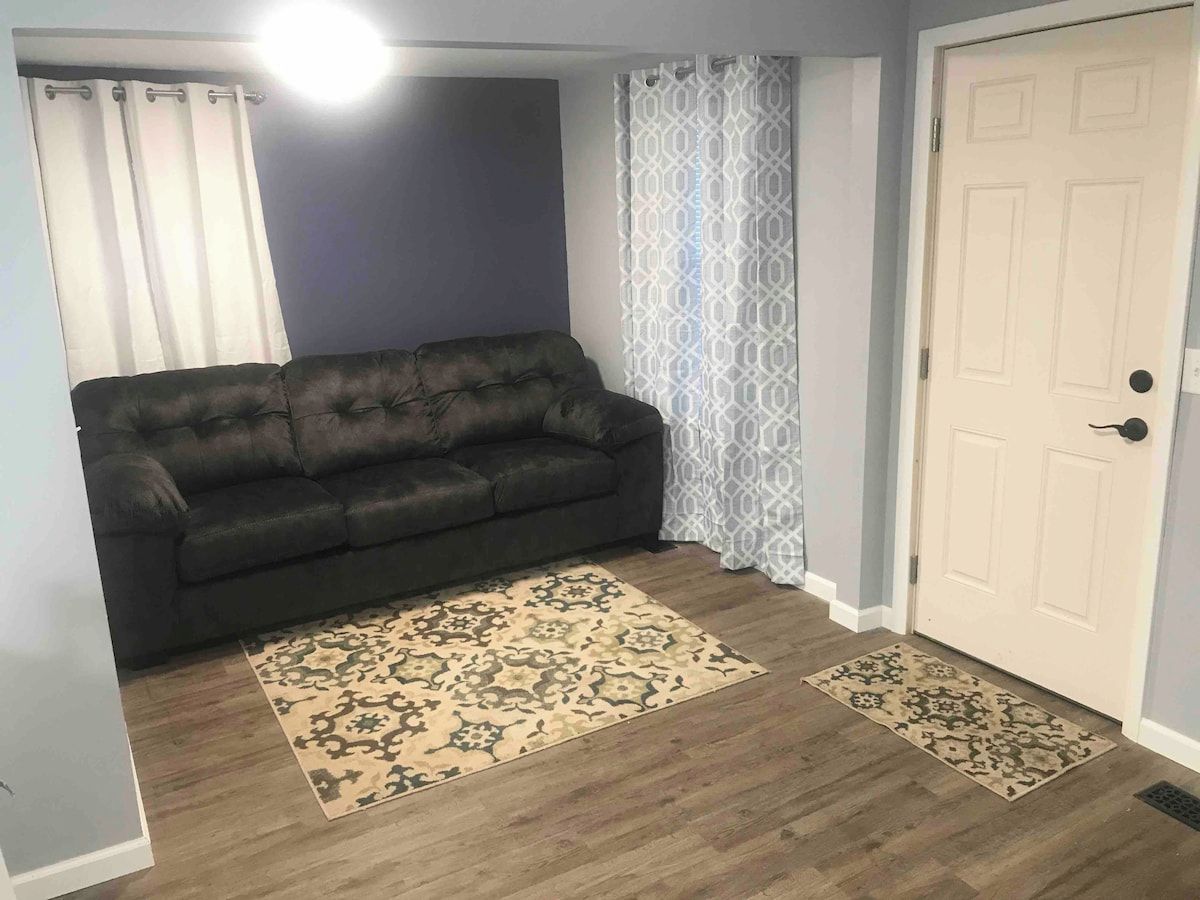 Ein Wohnzimmer mit einem dunkelgrauen Sofa, gemusterten Teppichen und einer weißen Tür.
