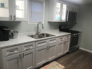 A kitchen with a double sink, stainless steel appliances, and white cabinetry. - Cozy One Bedroom House (Adrian)