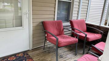 A porch with four red chairs and a wooden floor.