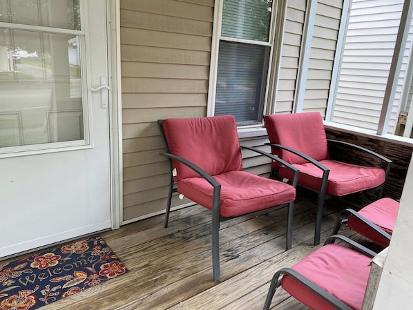 A porch with four red chairs and a wooden floor. - Cozy One Bedroom House (Adrian)