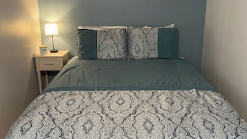 A bedroom with a bed, a nightstand, a lamp, and a wall-mounted picture.