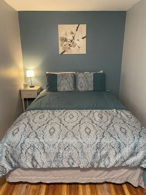 A bedroom with a bed, a nightstand, a lamp, and a wall-mounted picture.