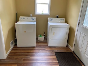 A laundry room with two front-loading washing machines and a small window above them. - Cozy One Bedroom House (Adrian)