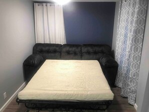 Una habitación con una cama, un sofá negro y una cortina.