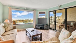Uma sala de estar com sofá, mesa de centro, televisão e porta de vidro deslizante para área externa.