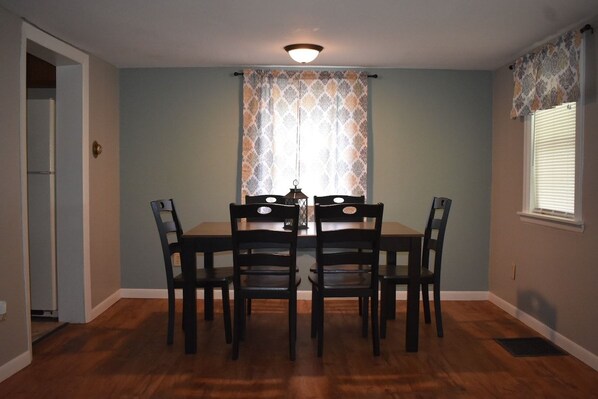 A dining area with a table and four chairs, a ceiling light, and patterned curtains.