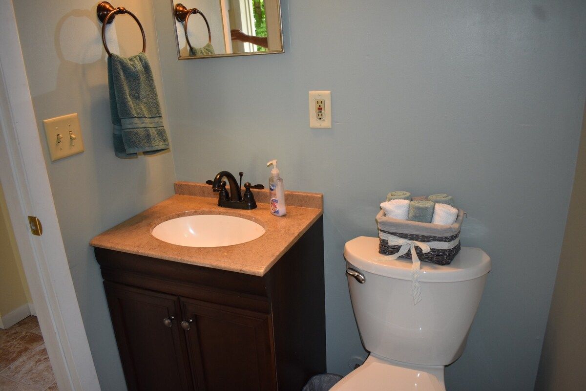 Une salle de bain avec un lavabo blanc, un meuble en bois foncé et des toilettes, à côté desquelles se trouve un panier rempli de serviettes pliées.